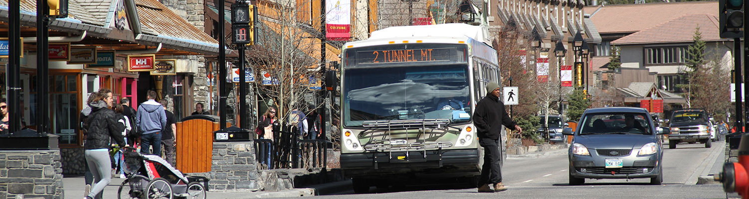 A hybrid bus waits for a pedestrian to cross in downtown Banff.