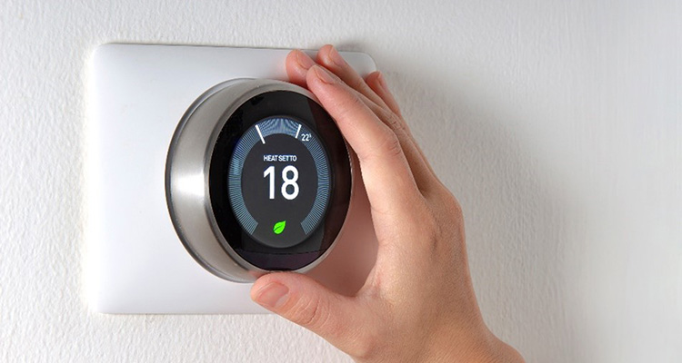 A hand turning the dial on a smart thermostat