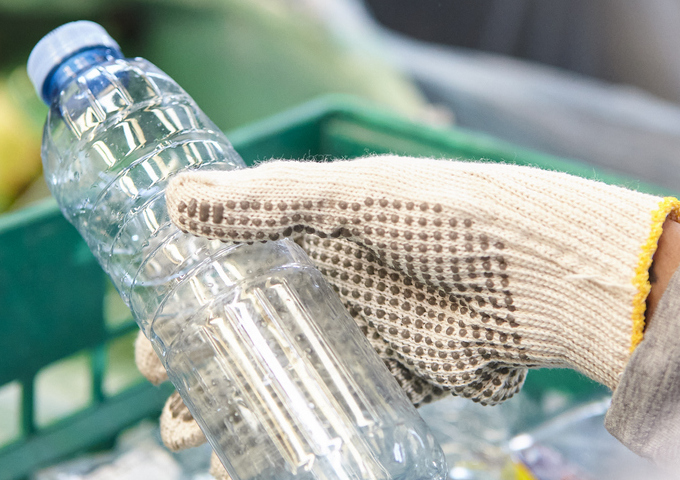 Teenager wearing grey sweater and plastic gloves sorts recycled water bottle 