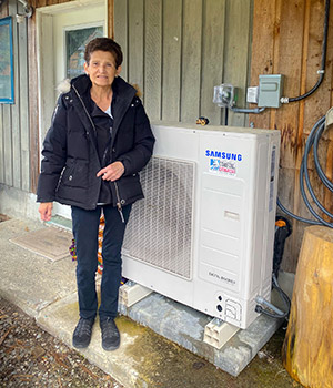 Une personne debout à l’extérieur à côté d’une maison et de l’unité extérieure du système de thermopompe.
