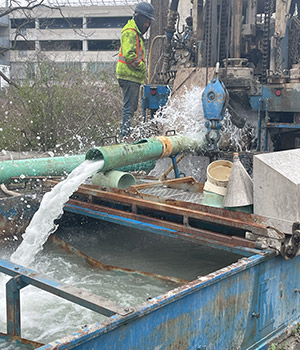 Un ouvrier portant un gilet de sécurité supervisant le fonctionnement d’un équipement technique, alors que de l’eau s’écoule d’un tuyau vers un réservoir