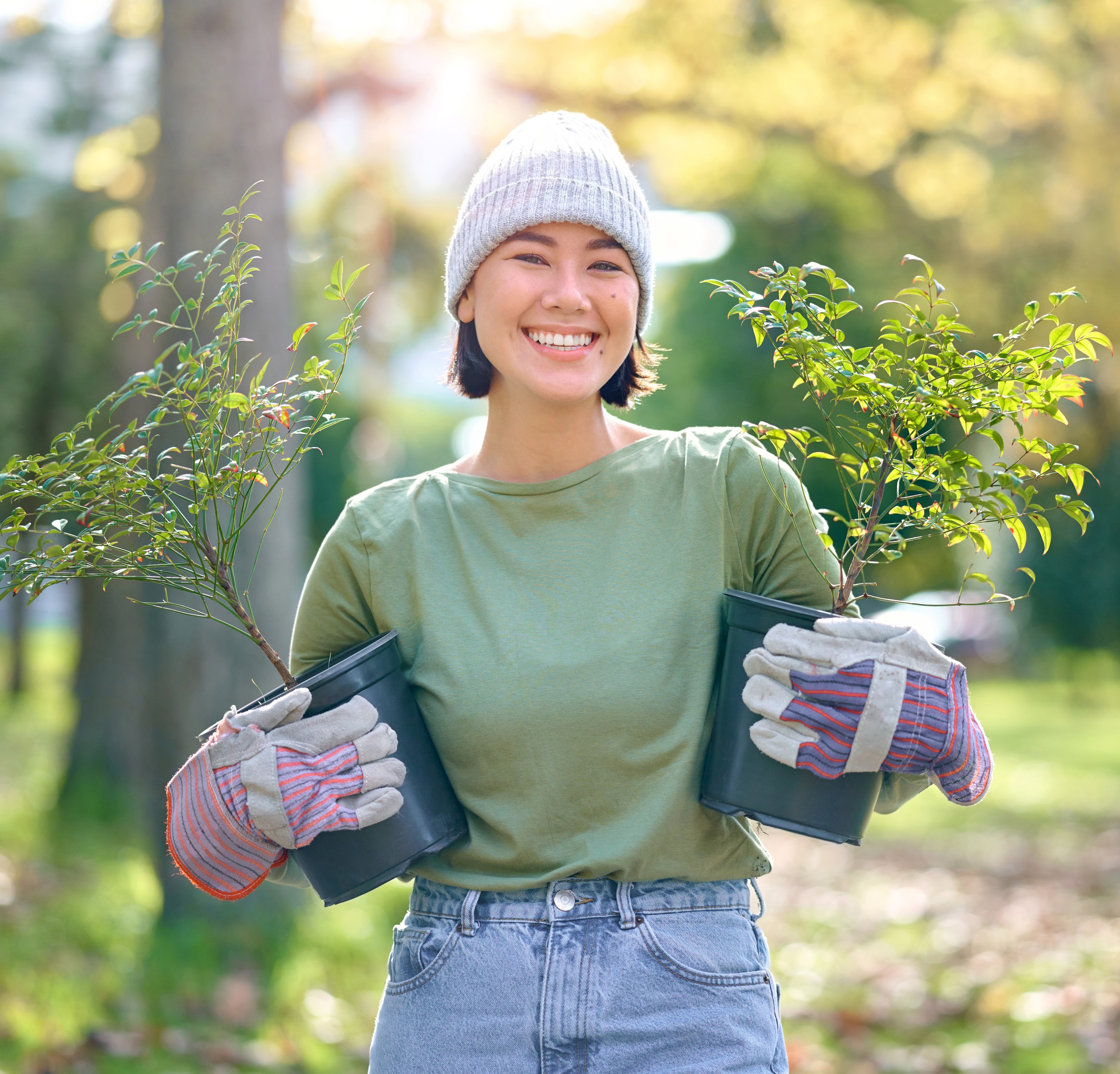 A woman smiling while holding two young trees