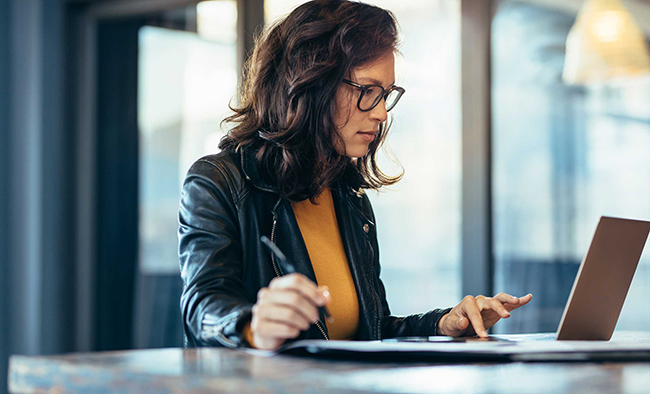 Business woman in glasses taking notes while working on a laptop. 