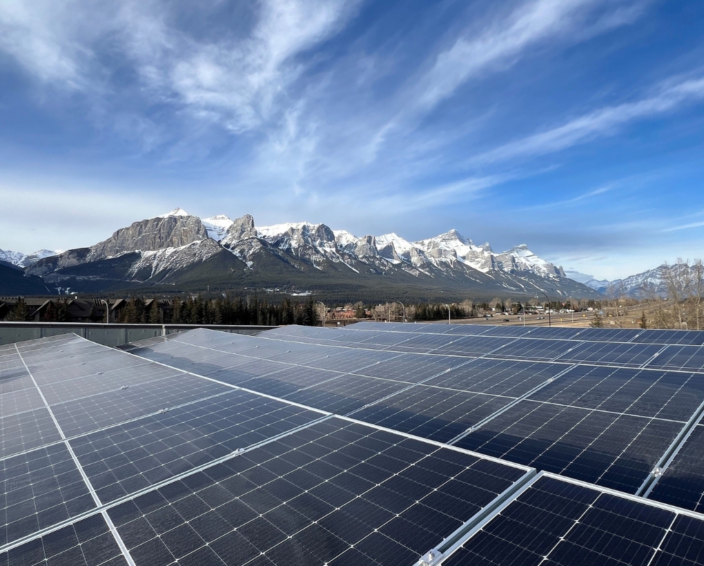 A view of rooftop solar panels with the snow-capped Rocky Mountains beyond.  