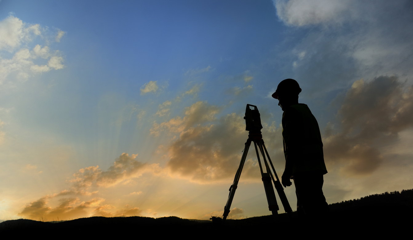 Silhouette of land surveyor working on a crested hill at sunset. 