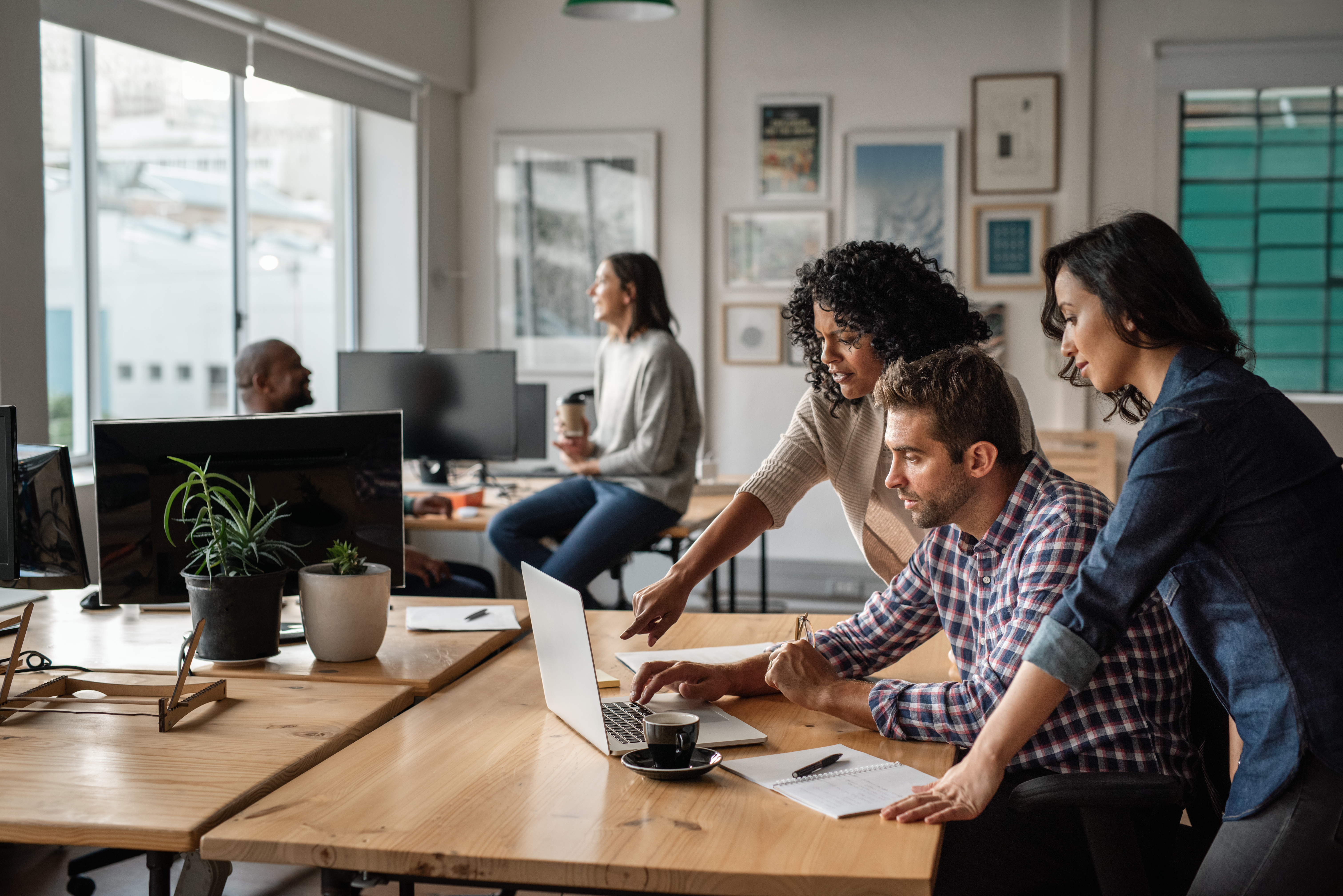 Group of casually dressed colleagues huddled around a computer in a bright, modern office.