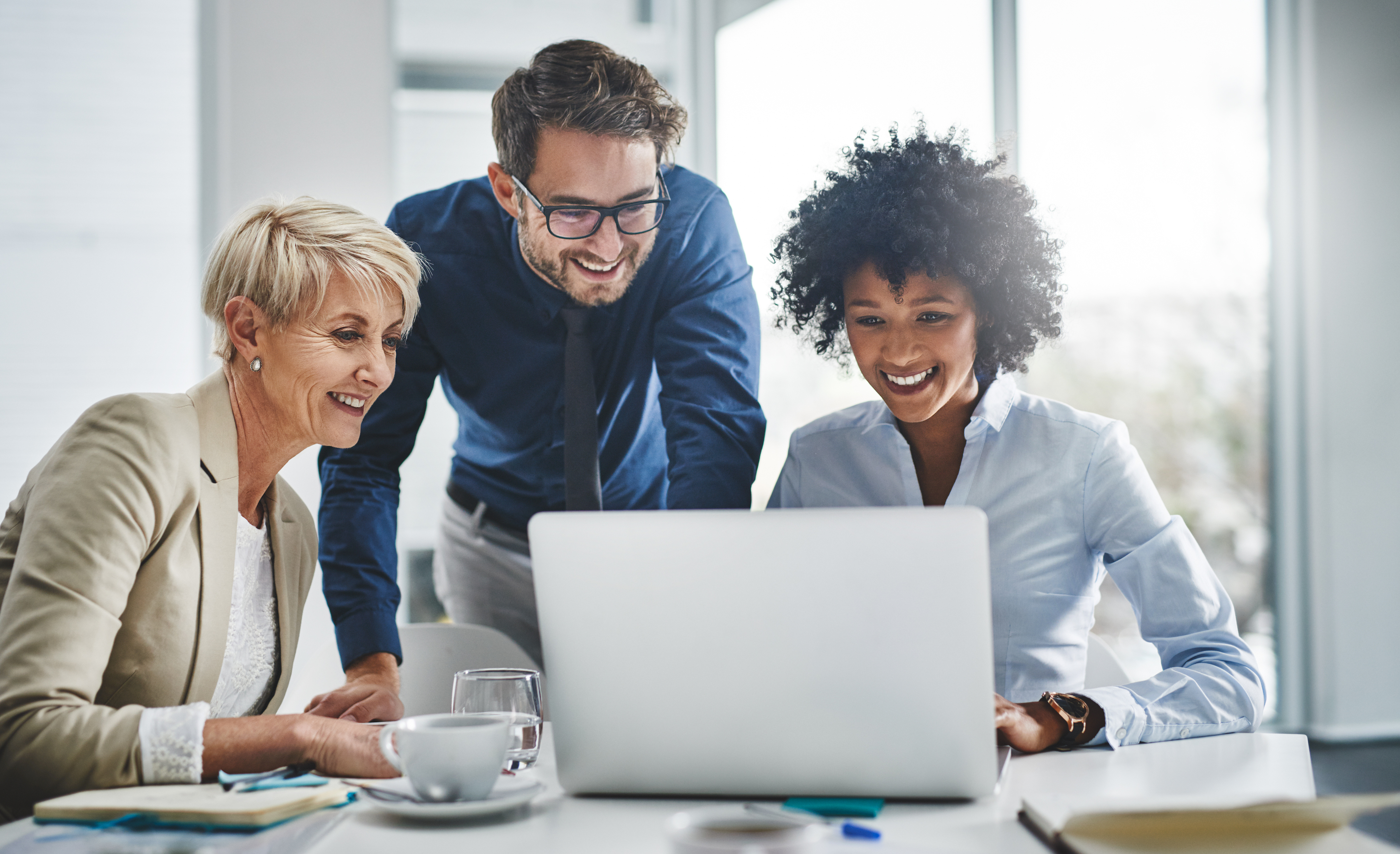 Two women and a man in business casual attire work on a laptop.