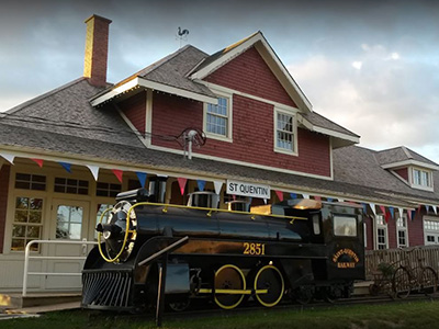 Une gare restaurée en rouge et blanc avec un train noir décoratif au premier plan.