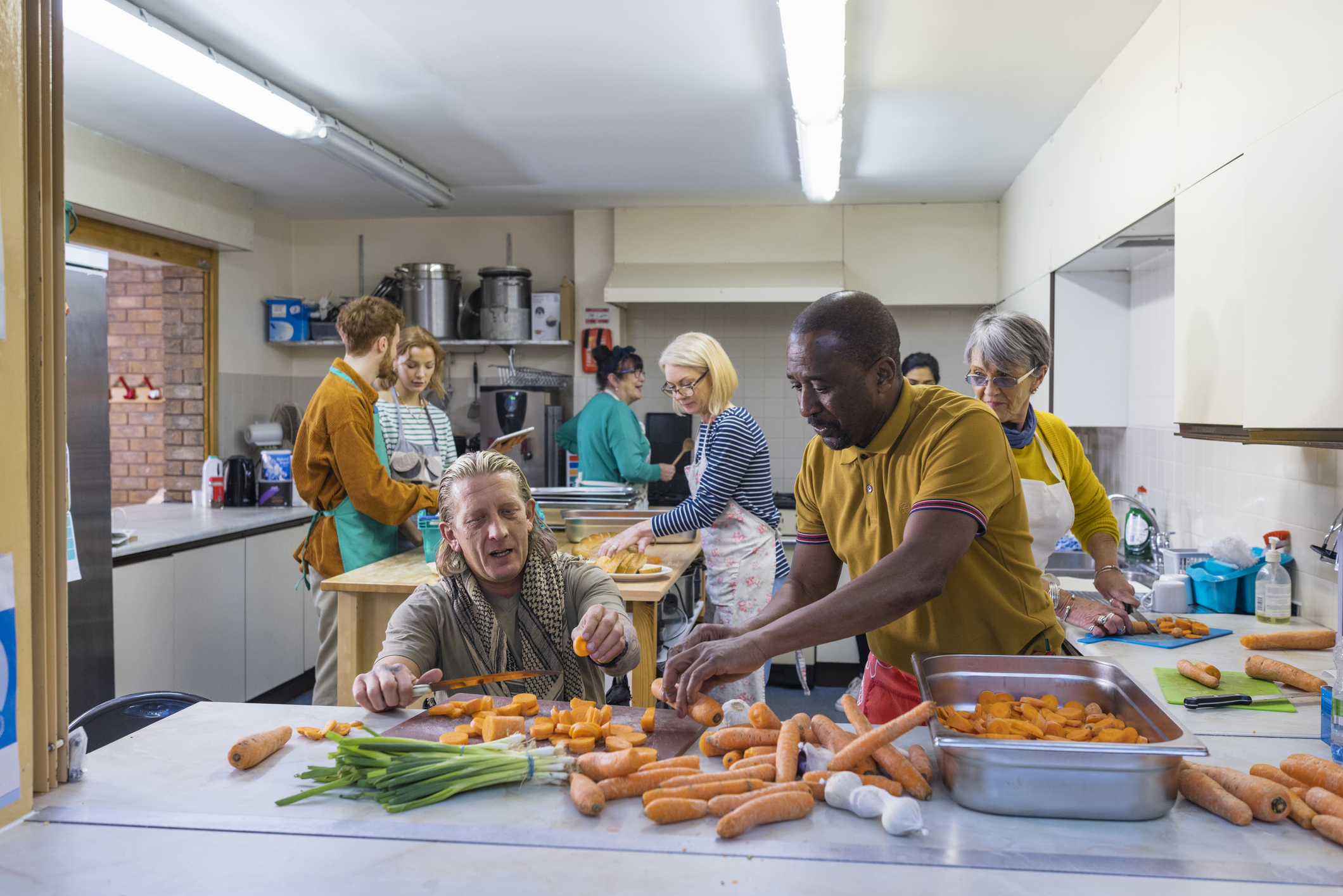 A diverse group of people cutting vegetables in a community kitchen