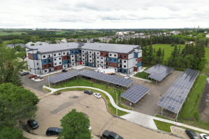 Aerial view of the final Muriel Ross Abdurahman Court housing complex, with solar panels on the roof of the building and in the parking lot. 