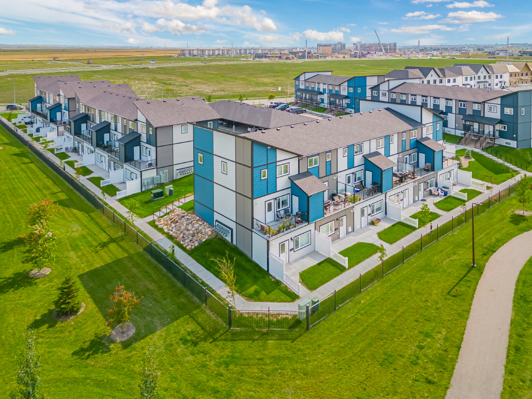 Vue aérienne grand angle du lotissement Aspen Heights à Saskatoon. Il s'agit de plusieurs complexes de maisons en rangée de deux étages, avec des panneaux extérieurs bleus et blancs et des toits en pointe bruns.