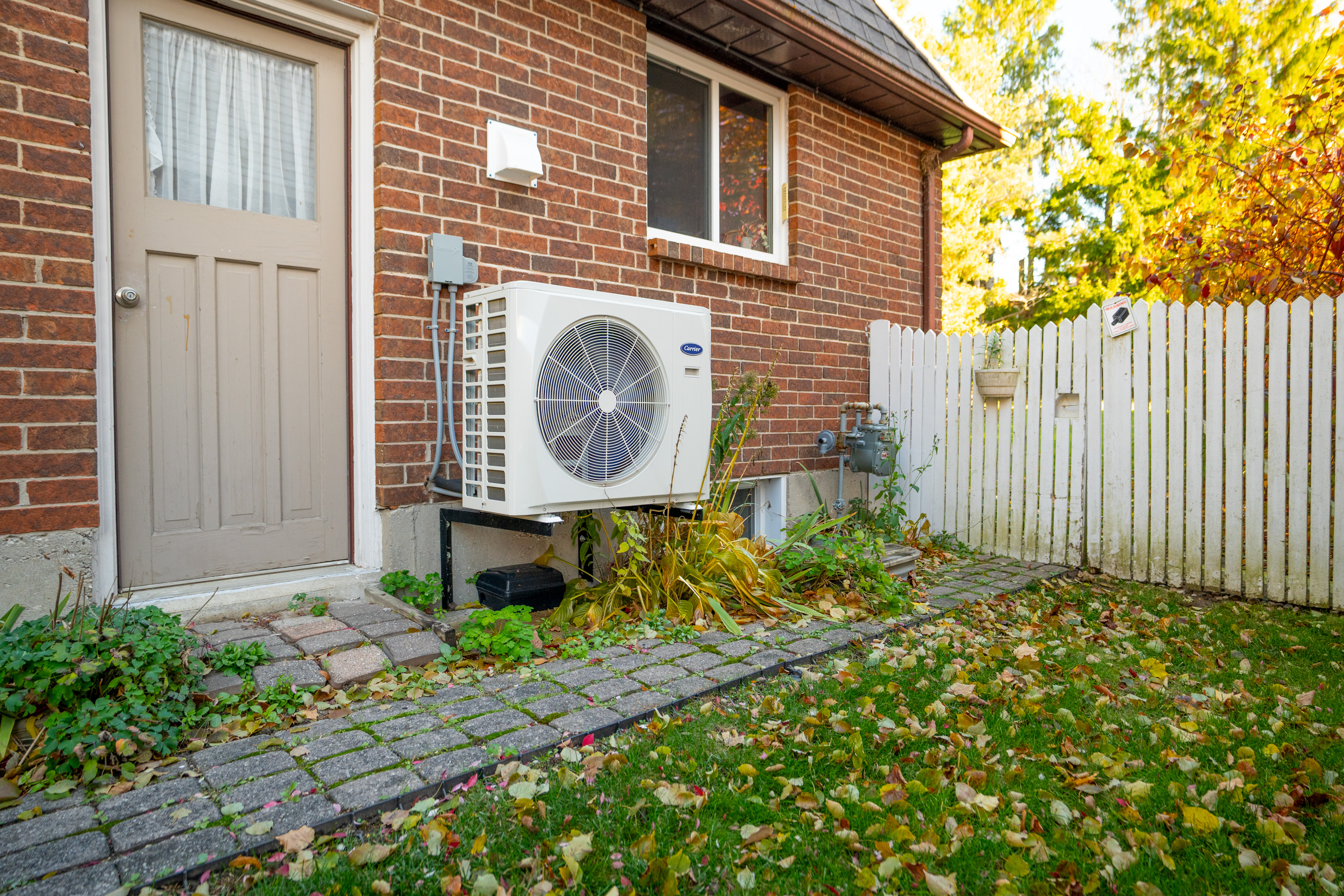 New heat pump on the side of a brick house in a small community.