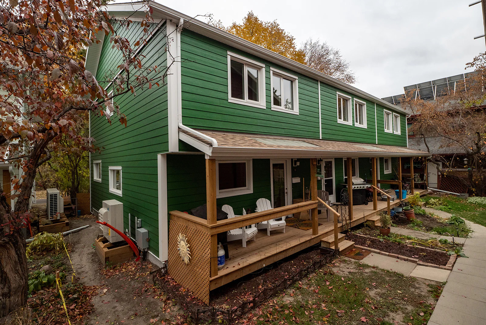 A view of a rows of townhouses at Sundance Housing Co-operative in Edmonton. The two-storey building has a green exterior, windows and doors with white trim, with a wood porch and a small grass lawn outside each unit.