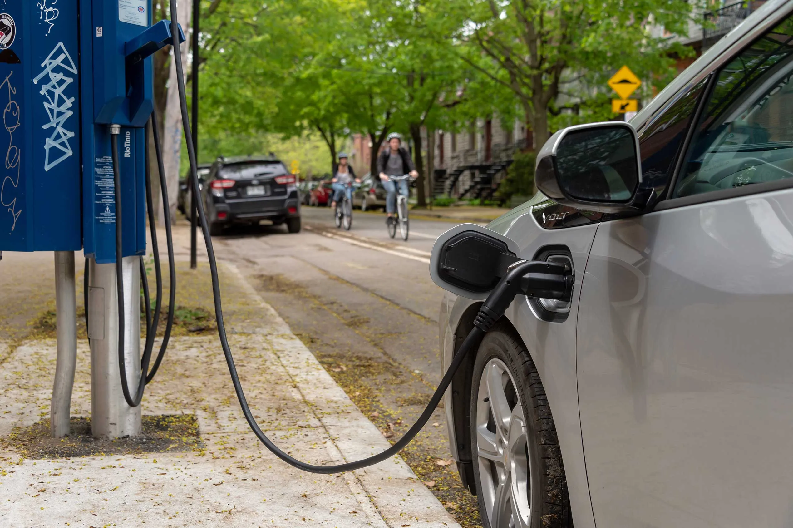 A silver car charges at an electric vehicle station on a residential street. 