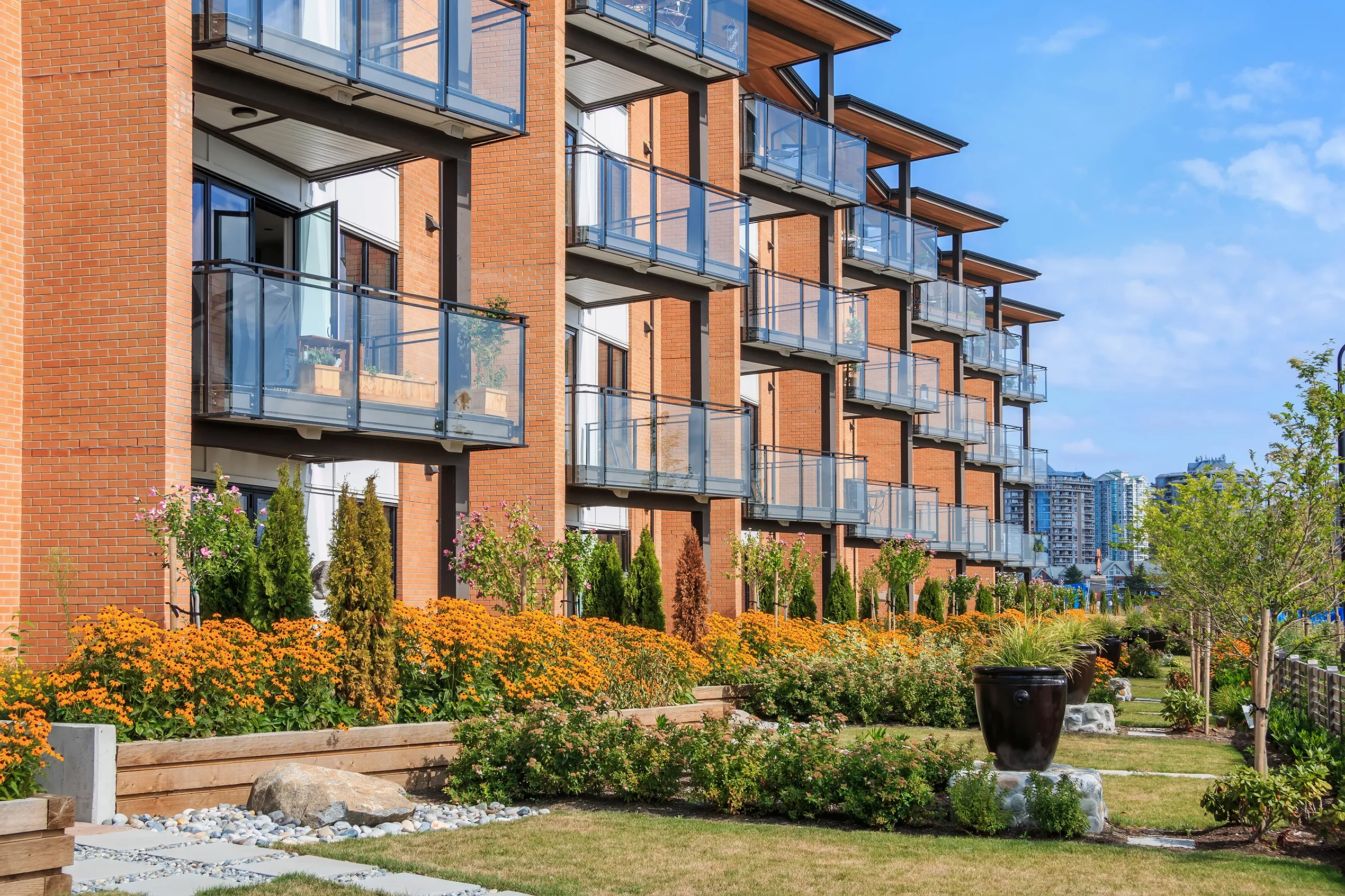 Angled photo of a modern four-story building with glass balconies, a clear blue sky, and a front yard greenscape.