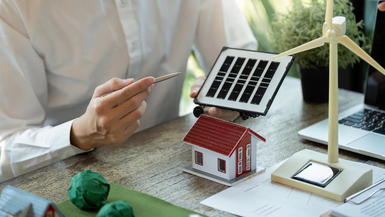 A person sitting at a desk with a model house, model wind turbine and a plan.