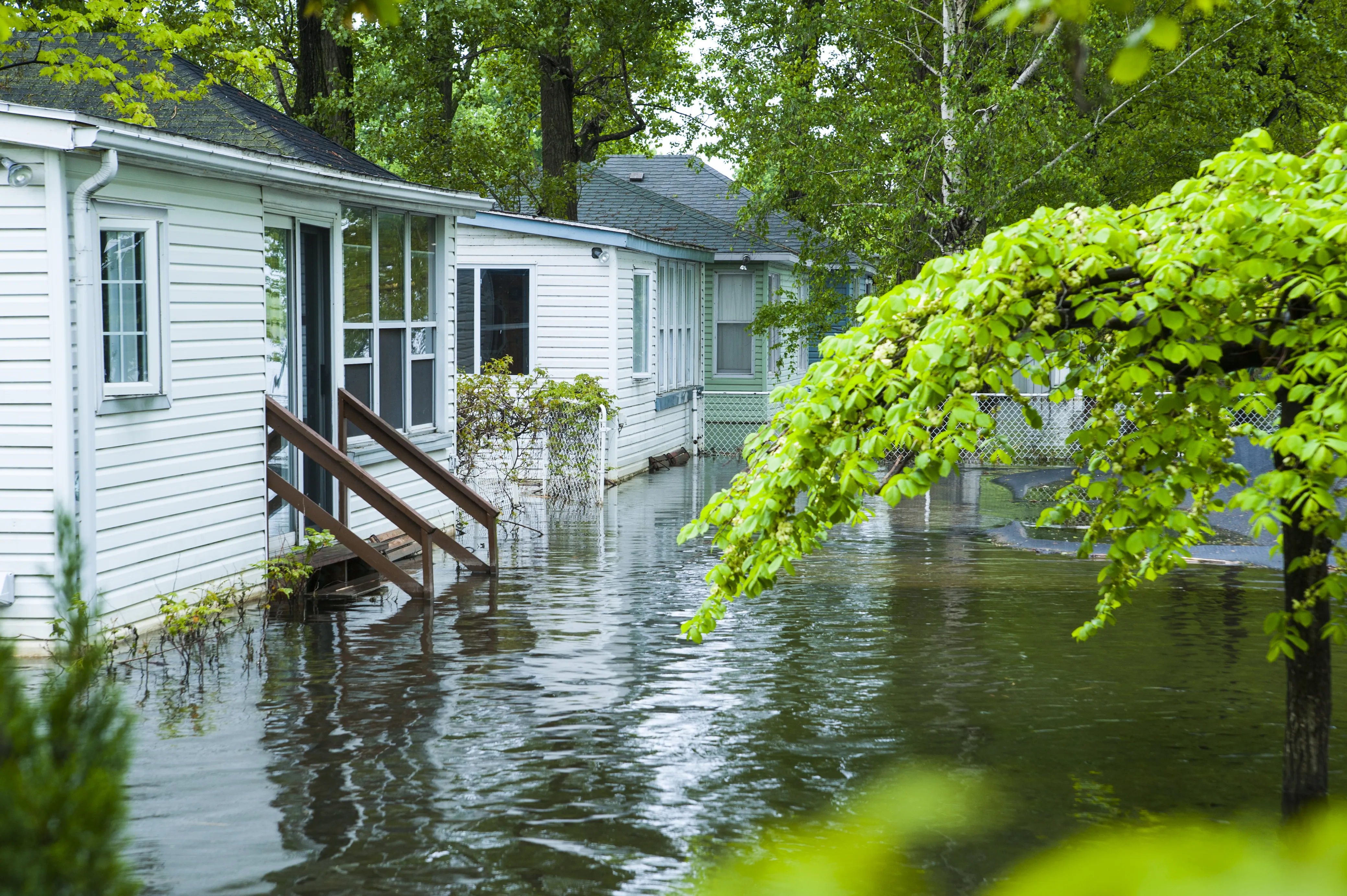 Flooded residential neighbourhood with rising water submerging yards and reaching the steps of houses, illustrating the impact of extreme weather and climate change on communities