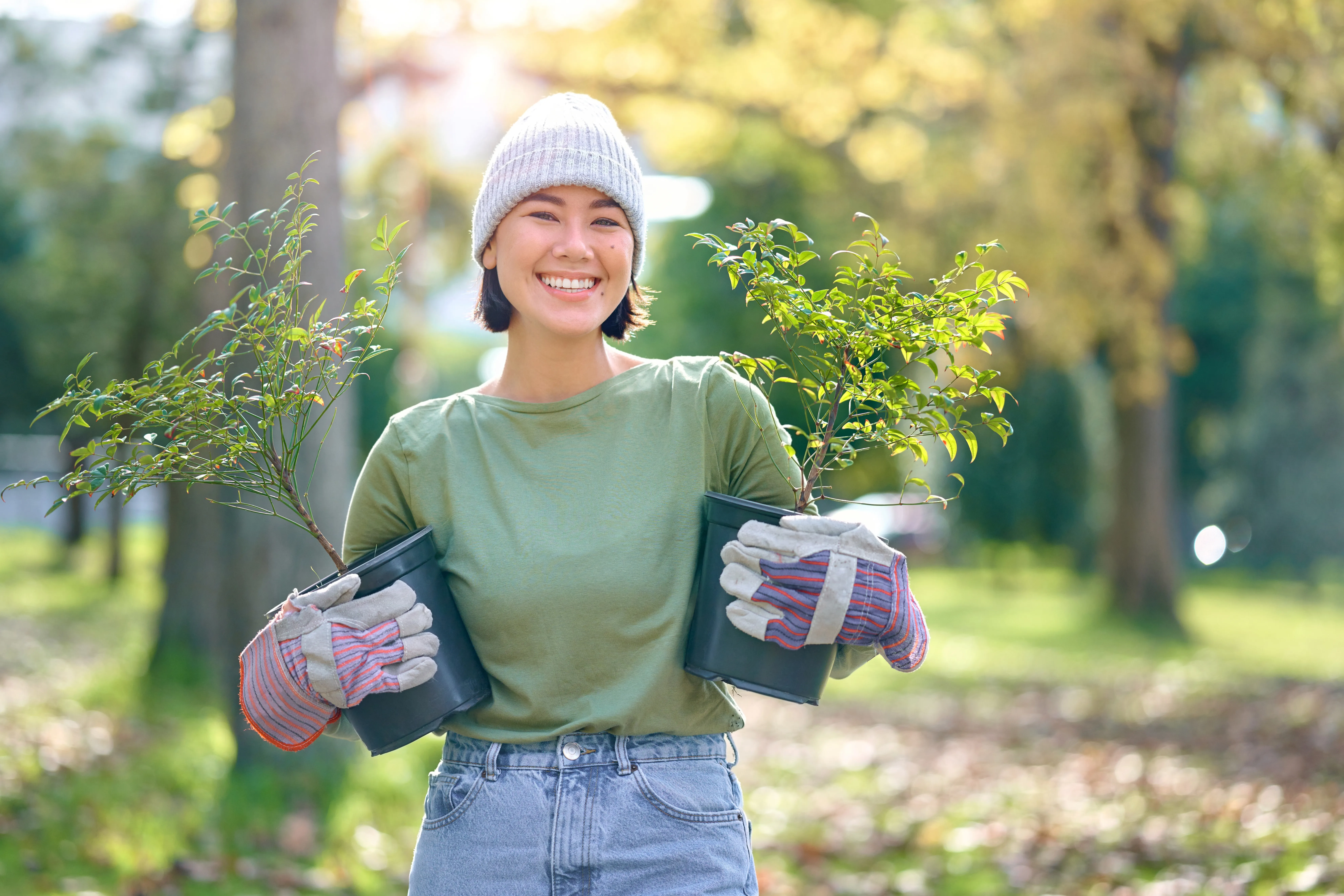 Sur un site de plantation, une accompagnatrice tient sous les bras deux arbres 