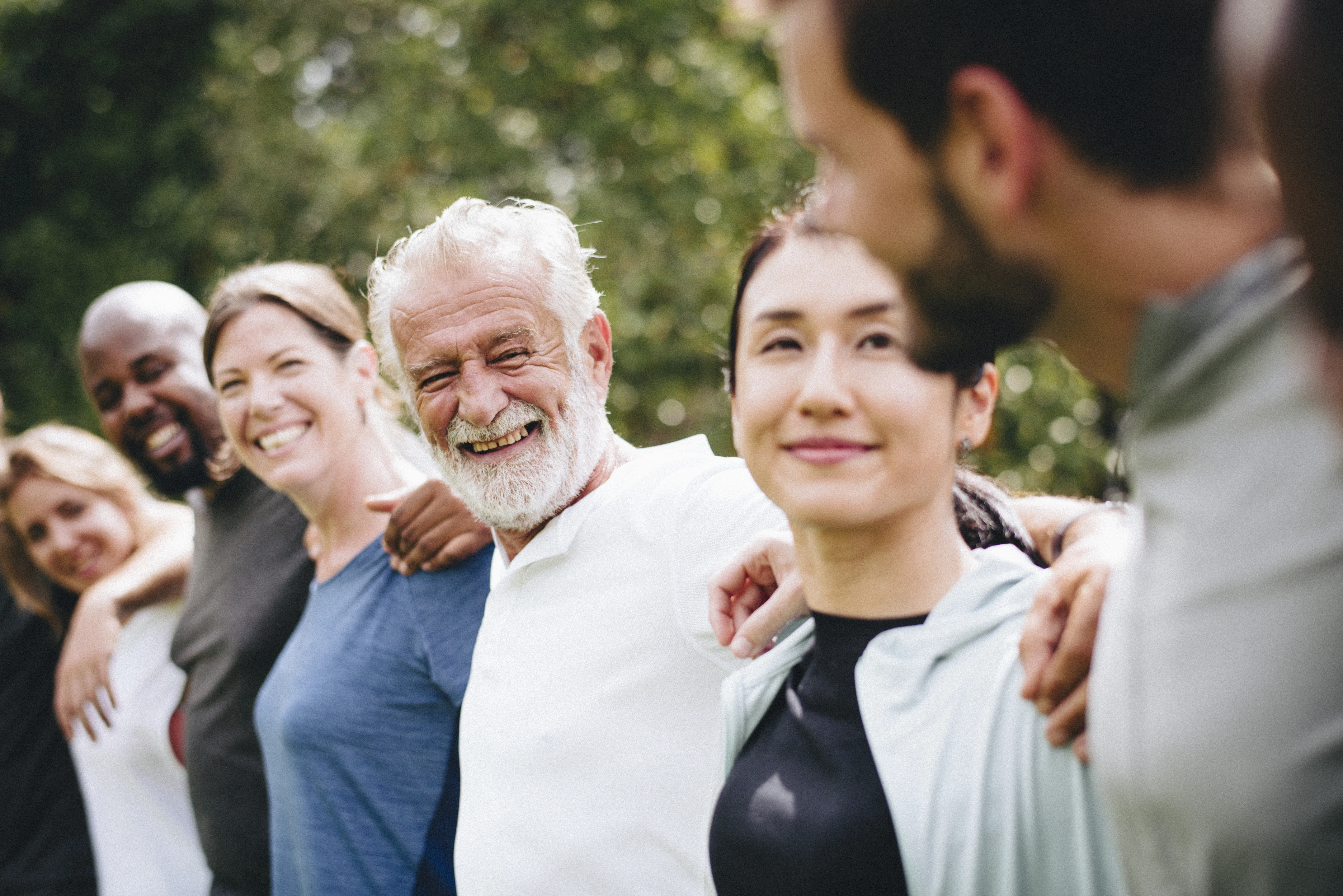Colleagues standing in a circle outdoors with arms around each other, smiling and connecting, symbolizing partnership and collaboration.