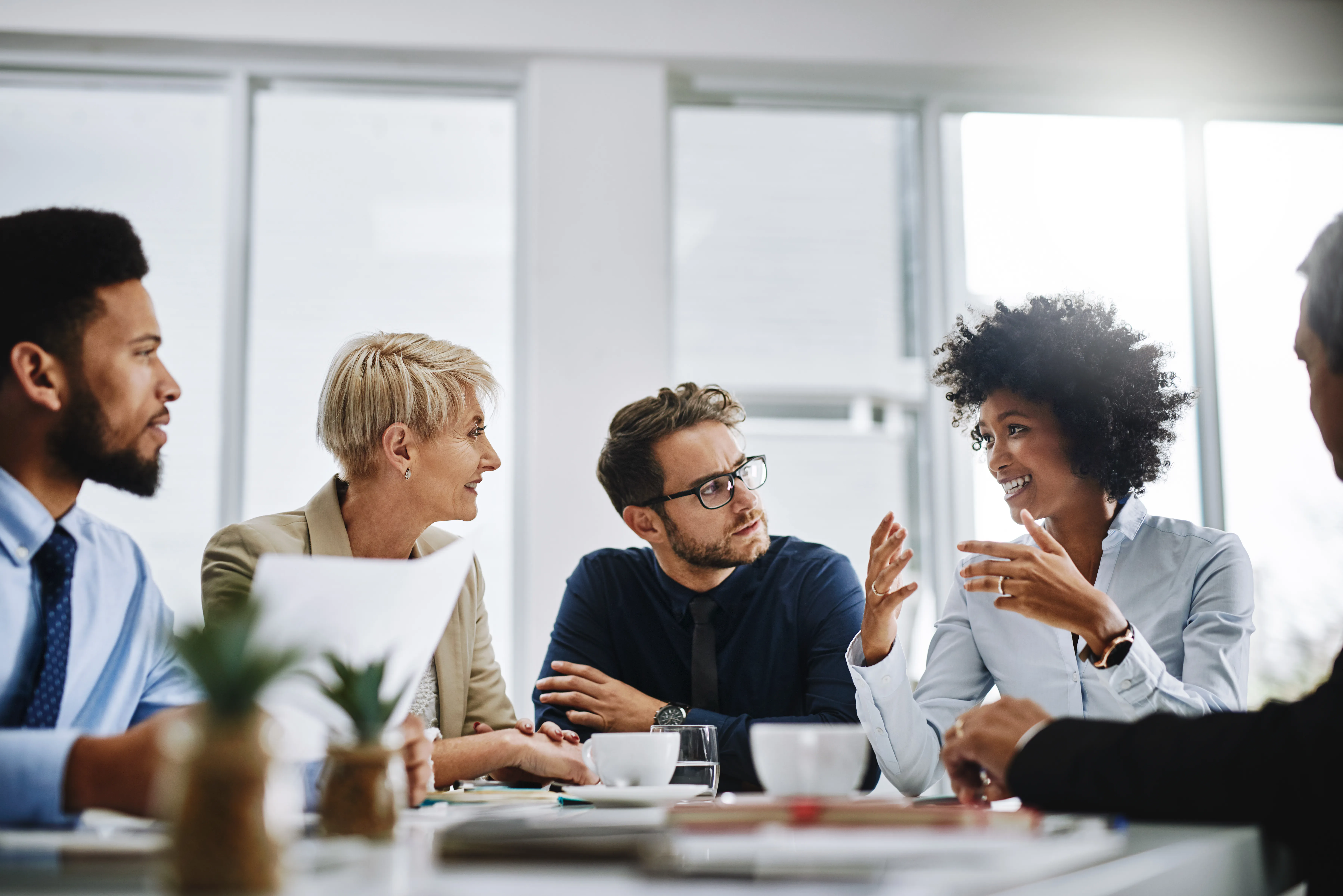 A diverse group of professionals sitting together in a meeting room, discussing ideas and collaborating around a table. 