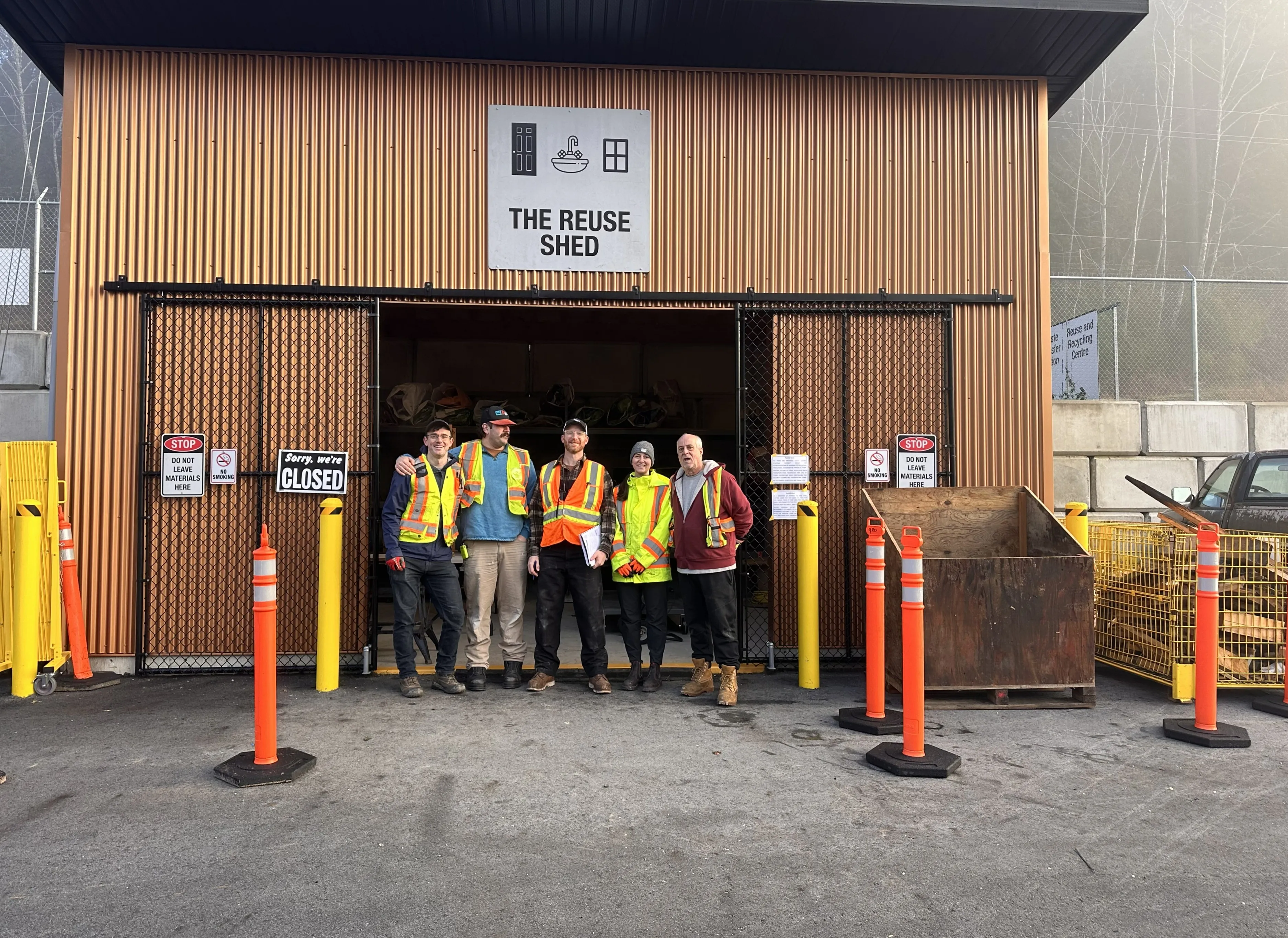 Group of employees in safety vests stand in the doorway of a brown wood-paneled building.