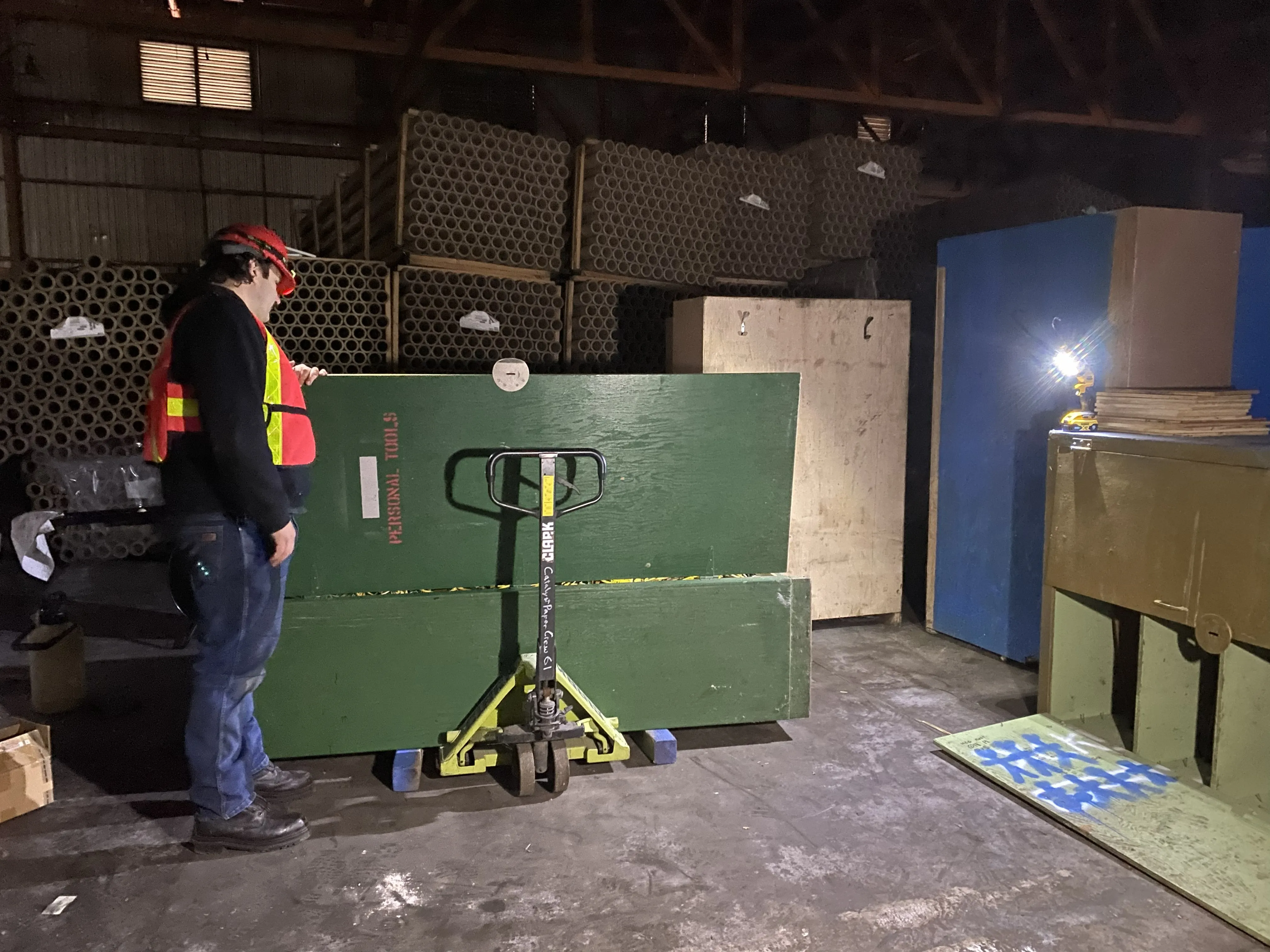Worker in red ball cap and orange safety vest stands inside an industrial space.